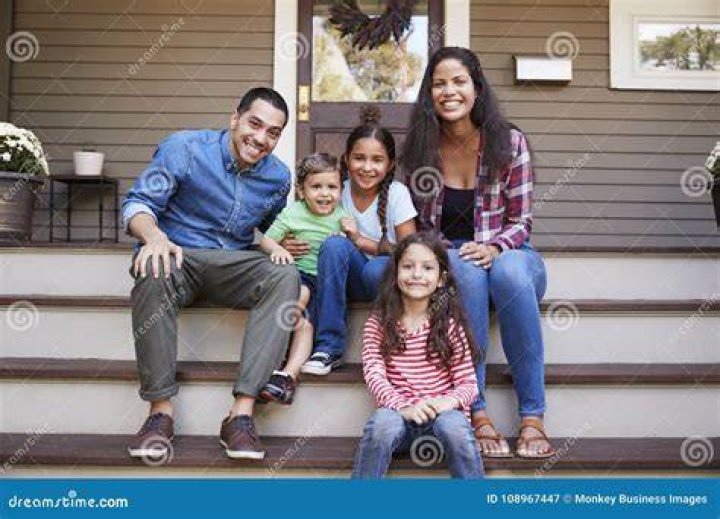 a family sitting on steps in front of some trees and bushes, posing for